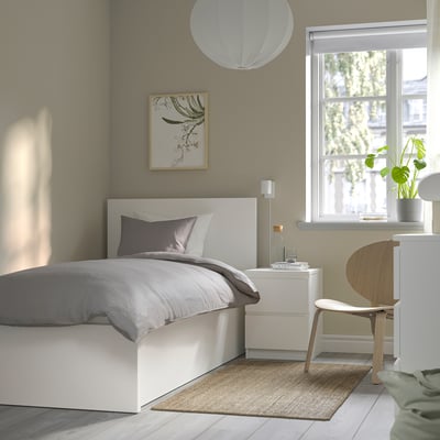 Minimalist bedroom with white MALM bed, grey linens, beige rug, floral art, and white light.