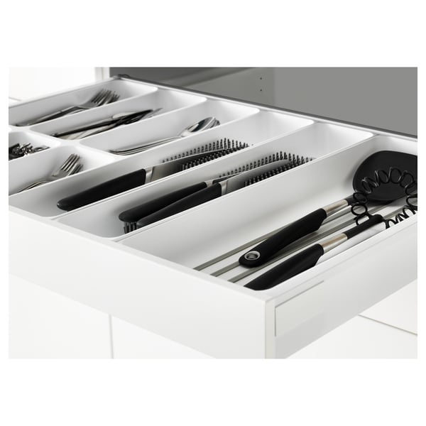 White kitchen drawer from METOD system, holding organised utensils, knives, and kitchen tools, with self-closing mechanism.