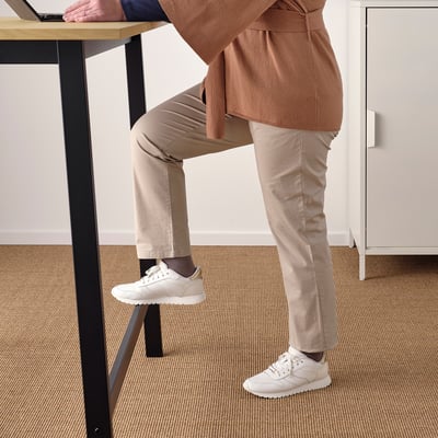Person standing at high table with footrest for support.