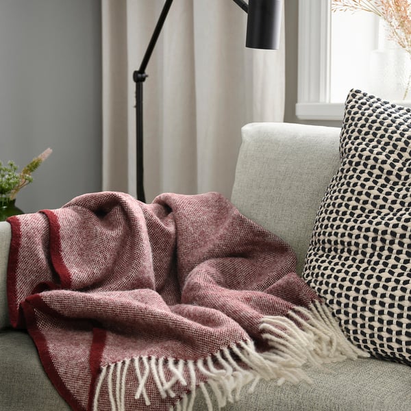 Cosy living room with a big red blanket and a patterned pillow on a light green couch.