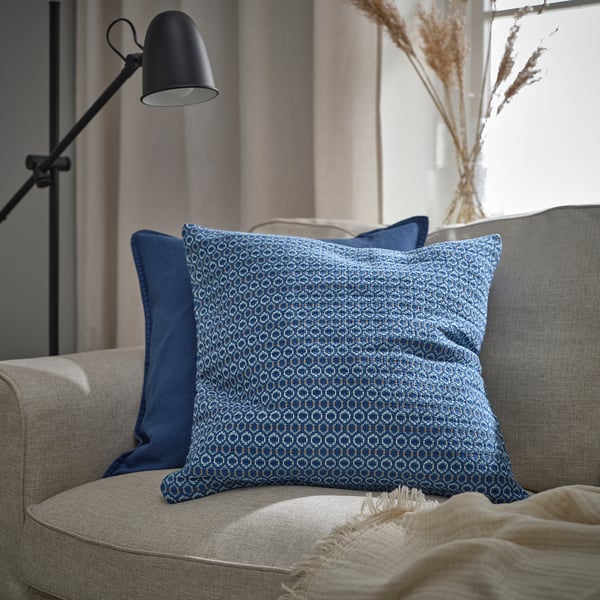 Modern living room with blue/grey MOROTSMOTT pillow on a beige sofa. Black floor lamp, beige curtains.