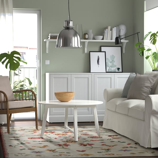 Living room with green walls, white furnishings, and NICKGRÄS rug. Coffee table and window enhance the cheerful atmosphere.