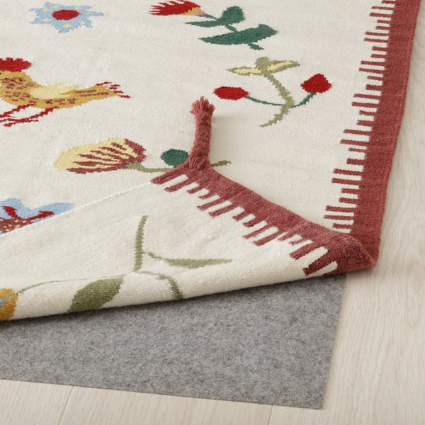 Colourful woven rug with flowers and small braids on corners, placed on grey underlay for safety and comfort.
