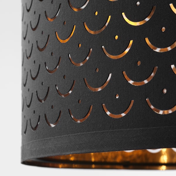 A black lampshade with intricate golden cut-out patterns of crescent moons and small circles, emitting a warm glow.