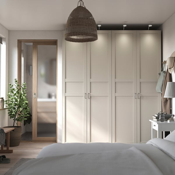 Minimalist bedroom light beige PAX wardrobes with soft-close doors, a woven pendant lamp, and a cosy bed with white bedding.