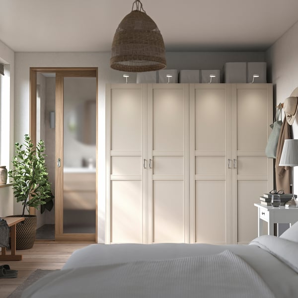 Modern bedroom with beige PAX wardrobe, grey rug, wicker pendant light, white bed, wooden floor, and houseplant.