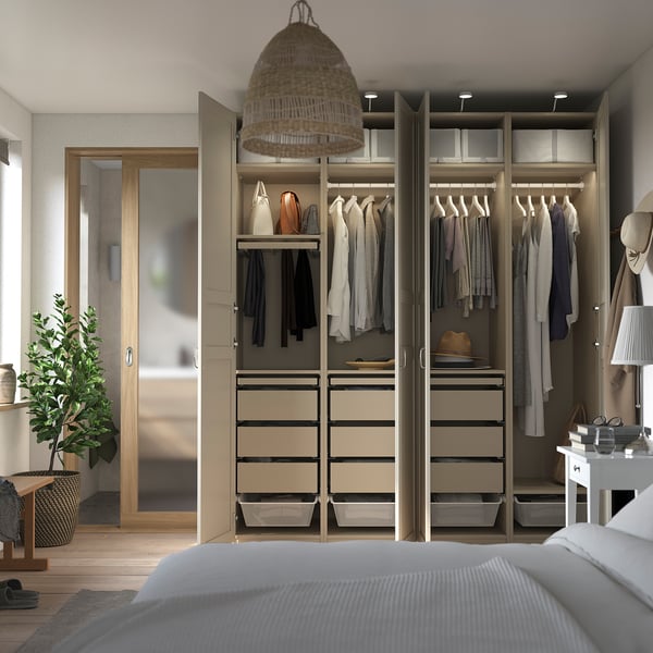 Modern walk-in closet with PAX system. Hanging clothes, shelves, and drawers. Light wood finish with soft lighting and a large mirror.