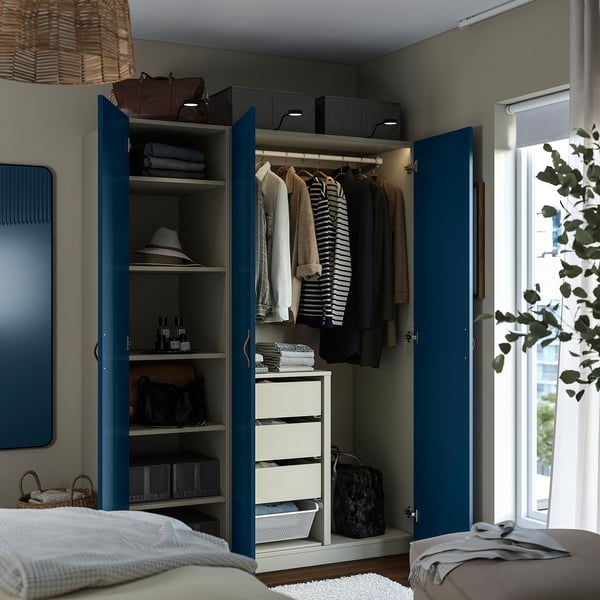 Open blue wardrobe with clothes, bags, and folded items on shelves and drawers. Integrated lighting at top.