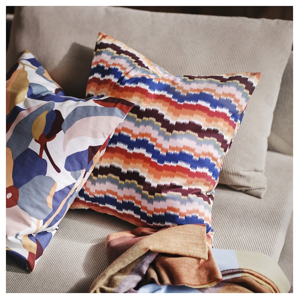 Vibrant cushions with zigzag design in warm colours on a beige couch. 3d shape, colourful patterns.