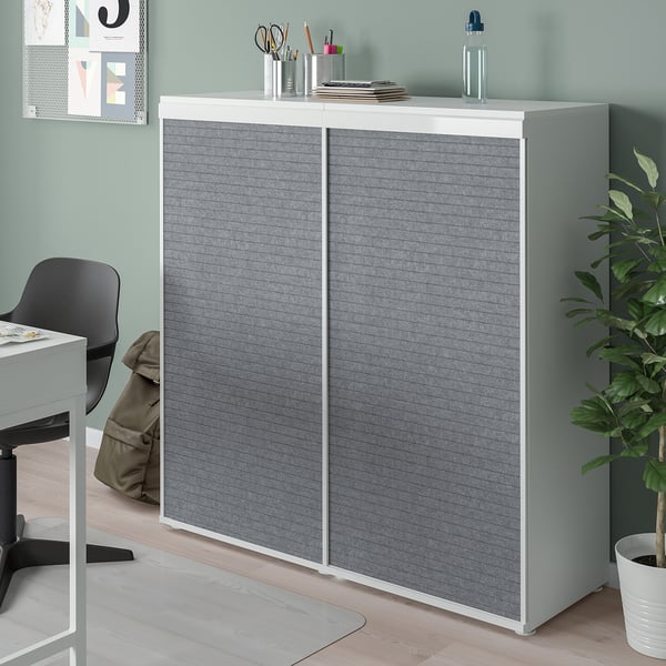 White PLATSA cabinet with grey doors in home office corner, taller than desk, housing items, plant beside it.