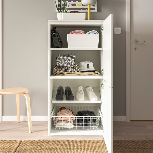 Open white storage unit, organised with shoes, bags, and folded clothes on shelves.