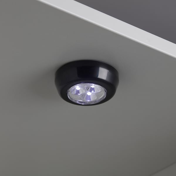 Small, round RAMSTA led light, black with clear cover, mounted on grey surface, emitting warm white light.