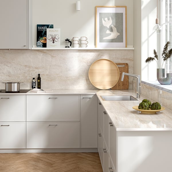 Modern kitchen with white cabinets, beige marble wall, wooden floor.