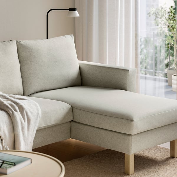 Modern, light grey sofa with chaise, wall light, cosy blanket, and coffee table with a book and remote.