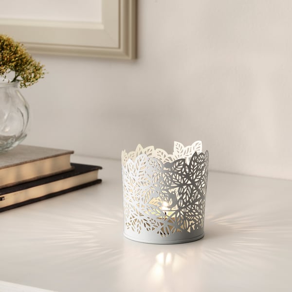 Tealight holder with leaf cutout, candlelit. Nearby, dried flowers and books create cosy decor.
