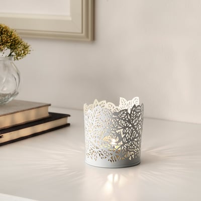 Tealight holder with leaf cutout, candlelit. Nearby, dried flowers and books create cosy decor.