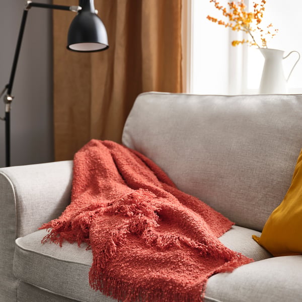 Living room with grey sofa, orange-red blanket, lamp, and orange flowers.