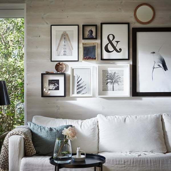 Modern living room with white sofa, decorative pillows, art wall frames, and a round coffee table featuring a vase with a single flower.