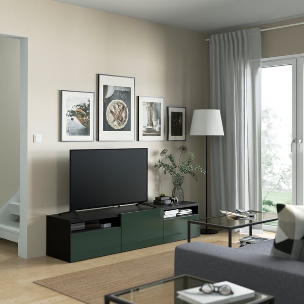 Modern living room with dark green tv stand, drawers, glass coffee table, grey curtains, and decor.
