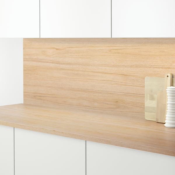 Wooden kitchen counter with light wooden panel backsplash, holding a cutting board and a small vase.
