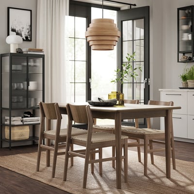 Modern dining table set with 4 wooden chairs, natural wood finish, round pendant light, surrounded by bookshelves and windows.