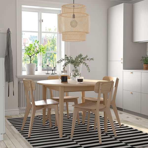 SKANSNÄS dining set with extendable round table, four armless chairs, pendant light, and black/white rug in bright kitchen.