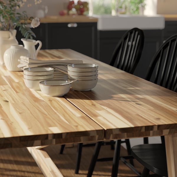 Wooden dining table with white bowls, black chairs, and a white vase with flowers, showcasing a simple yet elegant setup.