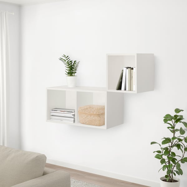 Modern living area with white walls, beige sofa, shelves with books, plant, and bamboo box. Floor plant near sofa.