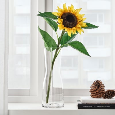 Sunflower in vase on windowsill with curtains.
