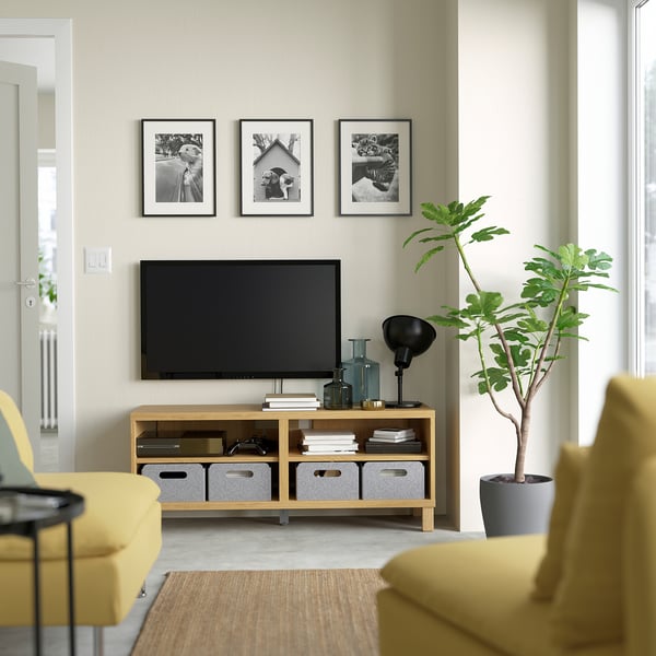 Clean living room with yellow couch, tv, plant, and photos.