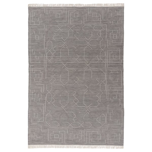 Depicts a grey TÅRGRÄS handwoven wool rug with a geometric pattern and fringed edges.