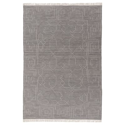 Depicts a grey TÅRGRÄS handwoven wool rug with a geometric pattern and fringed edges.