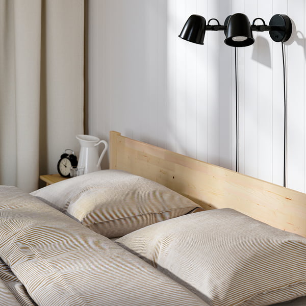 A cosy bed with a light wood headboard, striped pillows, and wall-mounted reading lamps.