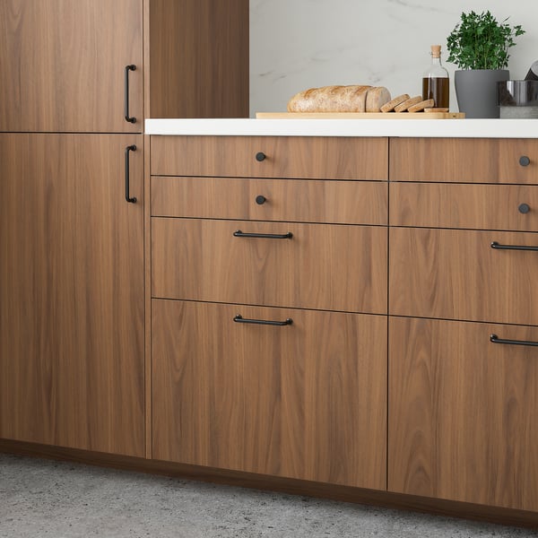 Modern wooden kitchen cabinets in walnut finish. Dark handles, narrow drawers. A loaf of bread placed on the countertop.
