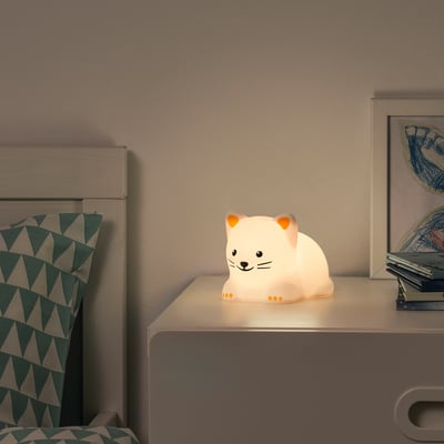 White cat night light on bedside table, small, glowing softly.