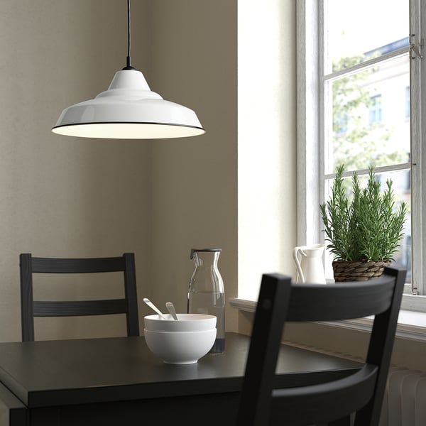 White TRETTIOEN lamp over dark table with chairs, bowl, and jug.