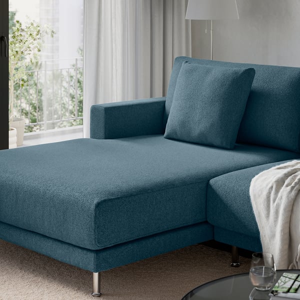 Modern blue sectional sofa with a chaise lounge, two cushions, and a lamp in a serene living room.
