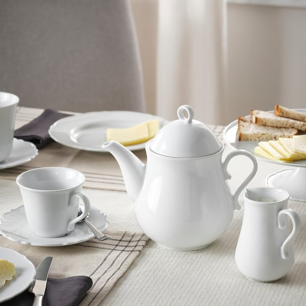 Table set for tea with white porcelain teapot, cups, butter knife, and sandwiches.