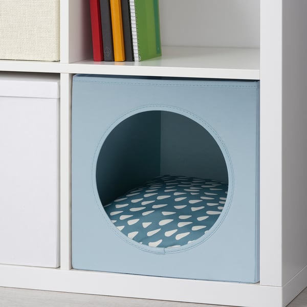 Pet cushion in blue fabric with circular entrance, housed in white shelving, perfect for small pets to rest and relax, providing comfort.