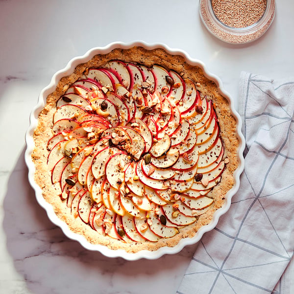 White wavy-edged pie dish with apple tart, on marble, striped cloth.