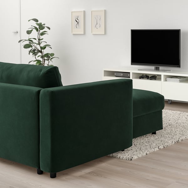 Modern living room with dark green VIMLE sectional sofa, tv, plant, and rug. Contrasts with white walls and light floor.