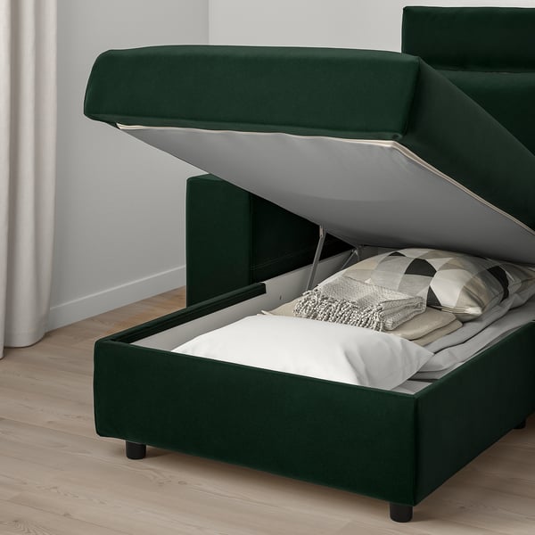 Modern green sofa with storage ottoman opened, showing bedding inside.