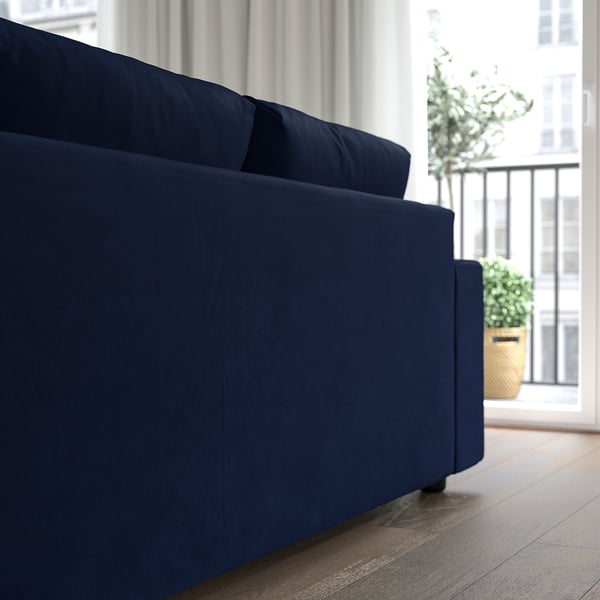 Bright living room with large blue sofa, big windows, plant, and light floor.