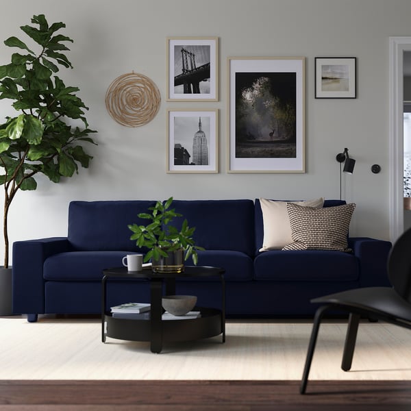 Modern living room with blue VIMLE sofa, wood coffee table, wall art, and large plant. Sofa fits well in space.