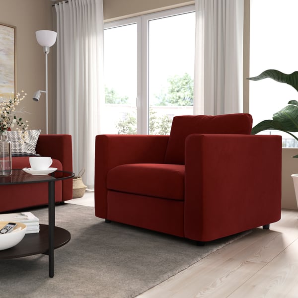 Modern living room with two red VIMLE armchairs, cushions, side tables, and large window. Soft lighting, and a grey area rug. Cosy and stylish.