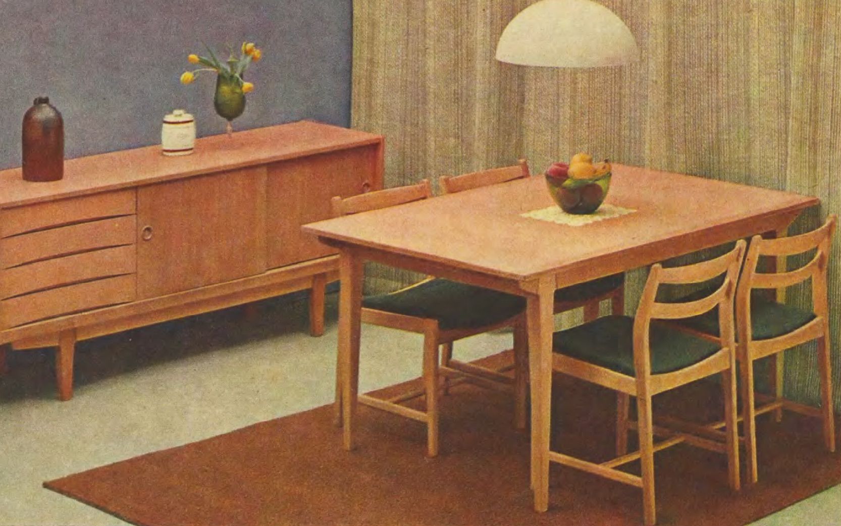 A sparsely-furnished dining area room set from 1965 with a sideboard unit and dining table styled with a bowl of fruit.