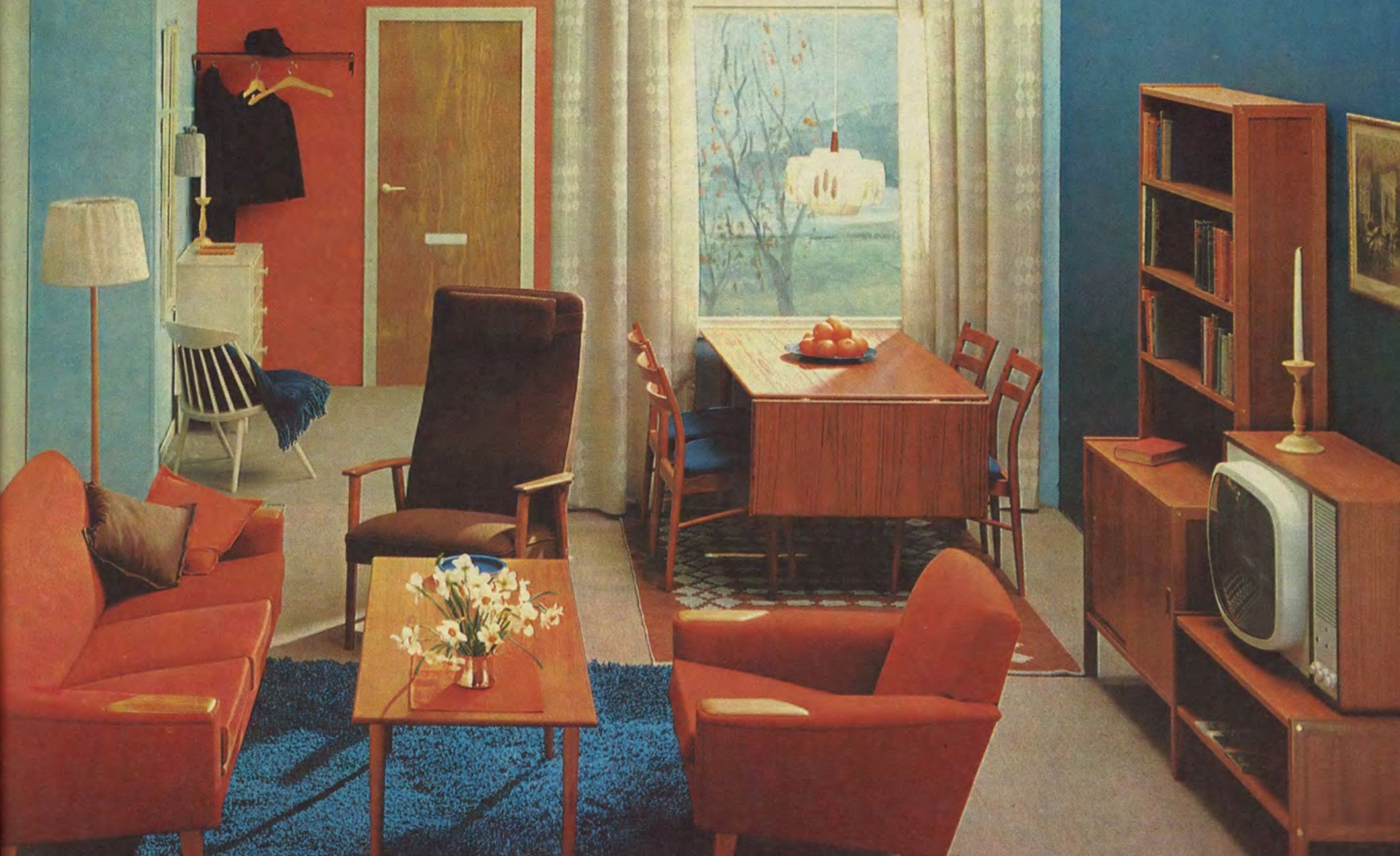 A bold blue and red/orange living/dining area room set from 1965, with a bowl of oranges on the dining table in the background.
