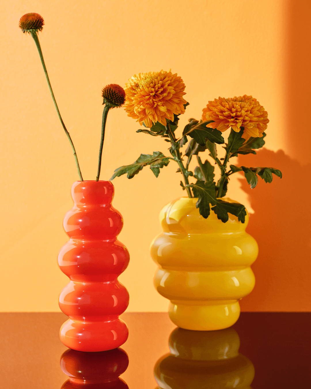 An orange background appears behind the cutout of two KÄLLARHALS vases filled with flowers.