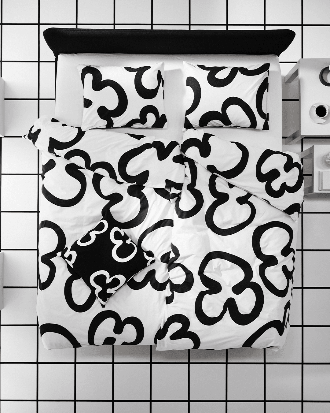 A cutout of a KLIPPBRÄCKA duvet cover and two pillows transforms into an aerial image of the bed linen on a bed, against a black and white windowpane check roomset.