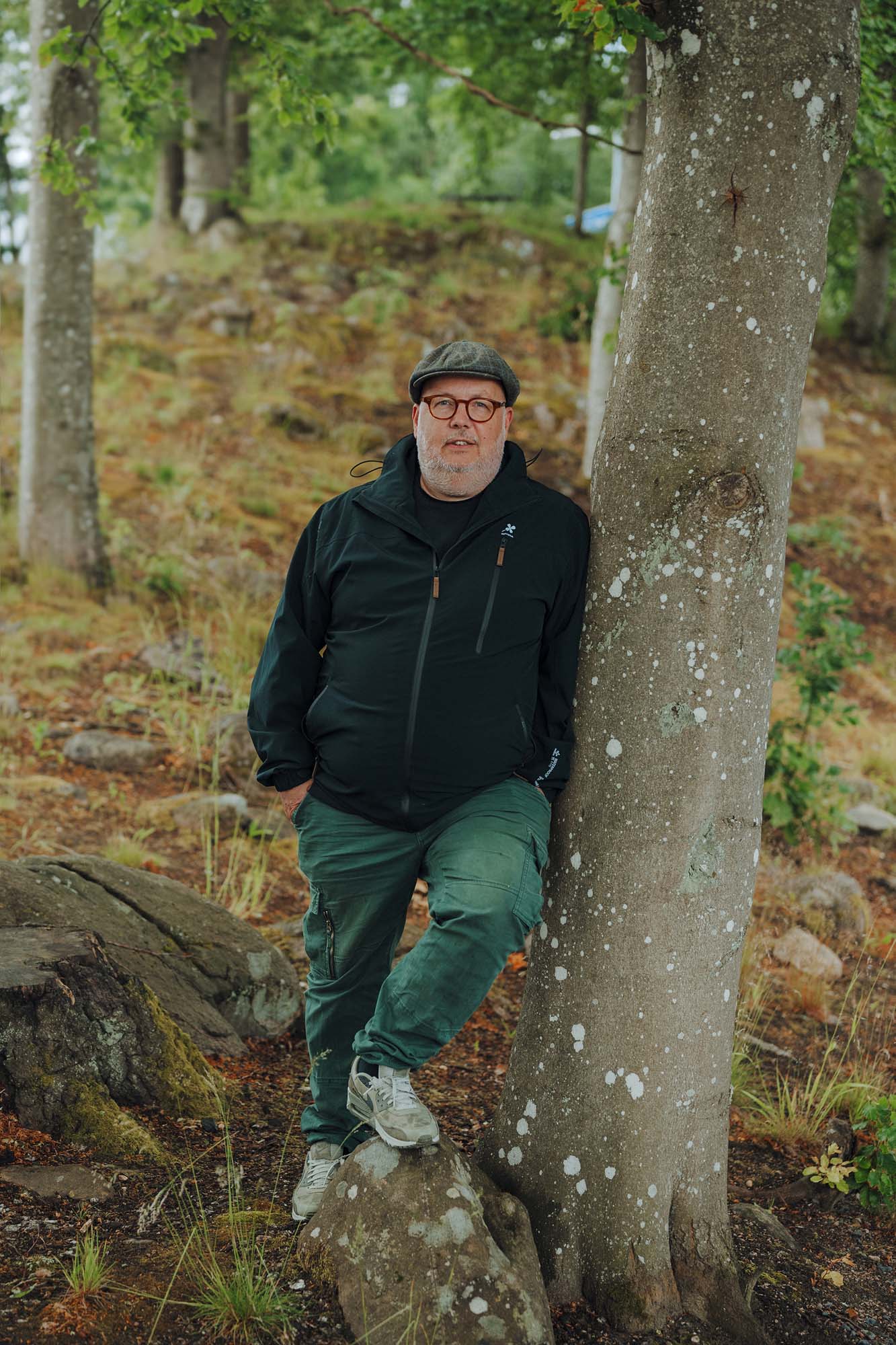 IKEA co-worker Erik Leupen stands outside and leans against a tree, with one foot perched on a rock.